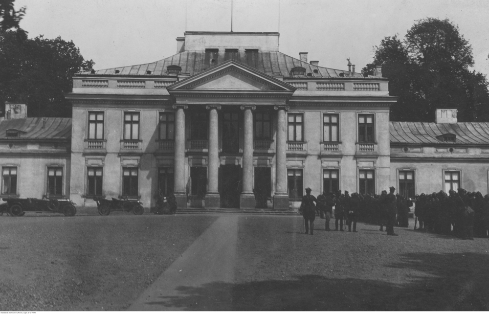 Fotografia przedstawia budynek Belwederu, stojących przed nim żołnierzy oraz zaparkowane samochody.