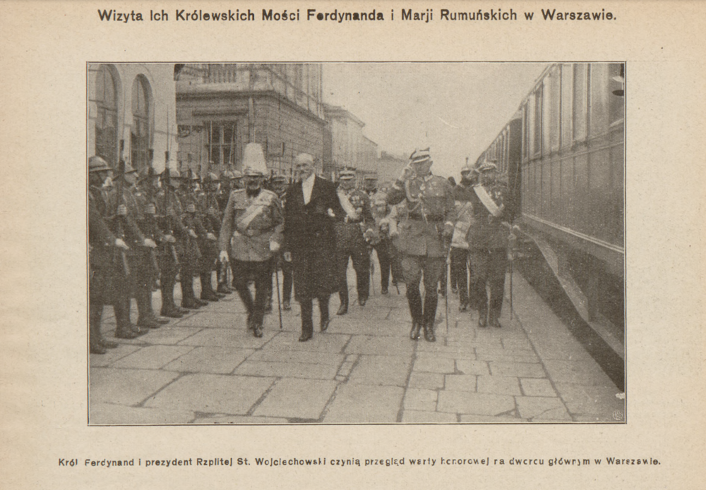 Fotografia przedstawia dworzec Wiedeński w Warszawie, po prawej stronie widoczne są częściowo wagony pociągu, po lewej natomiast żołnierze. W centralnej części fotografii widzimy króla Ferdynanda I oraz prezydenta RP Stanisława Wojciechowskiego.